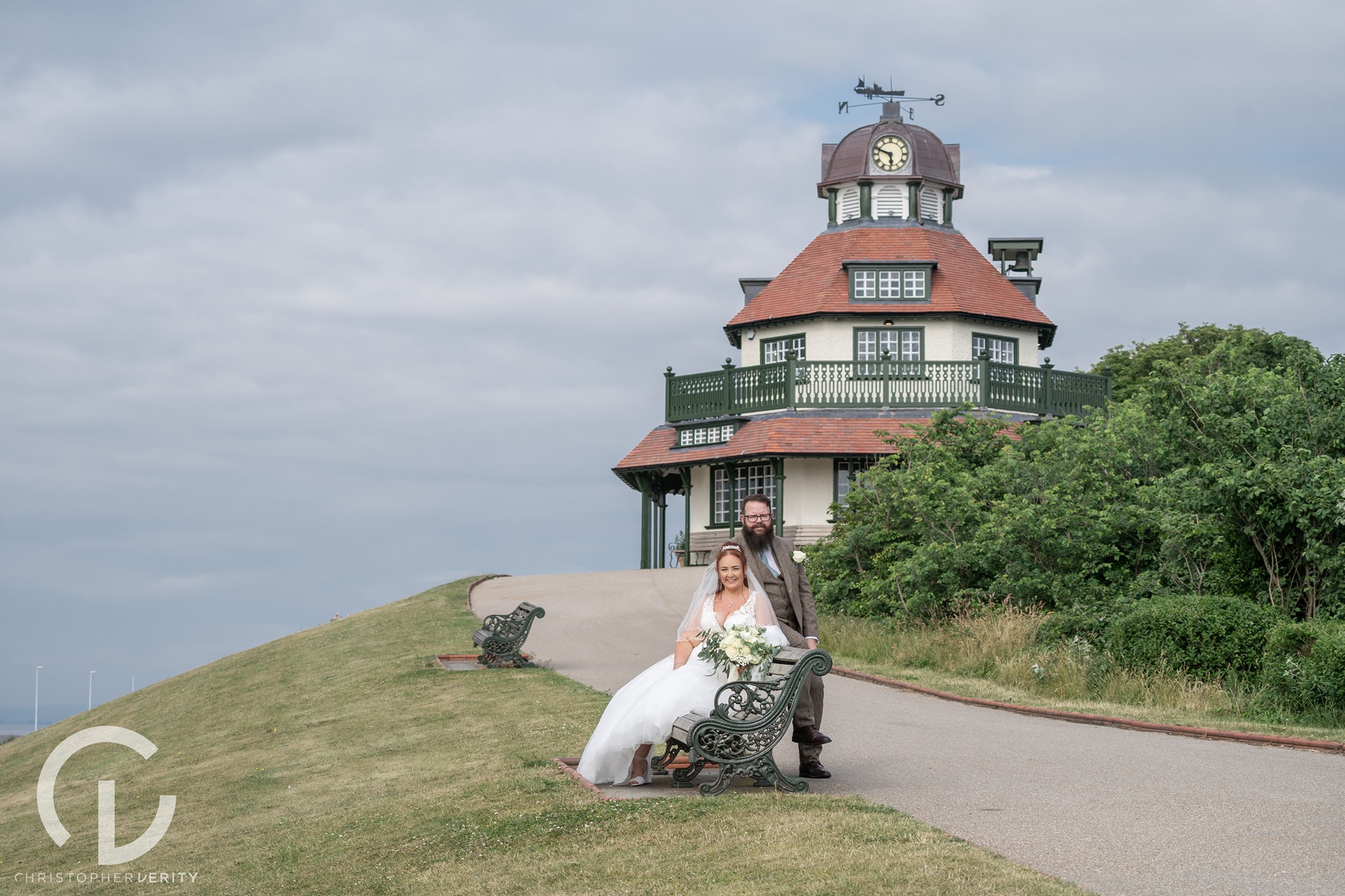 A couple in wedding dress sat on a bench in front of the Mount pavilion in Fleetwood